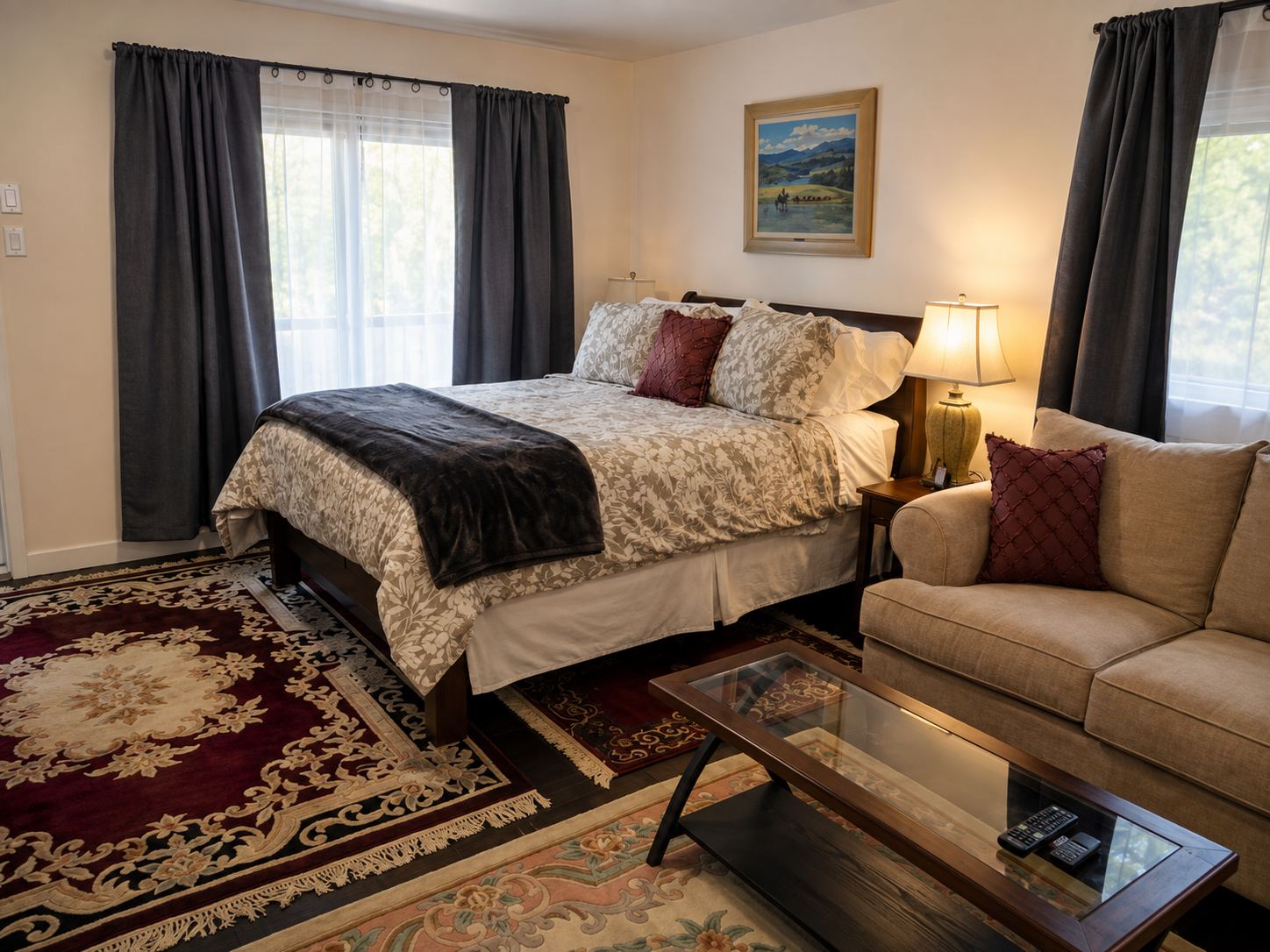 The Chilcotin suite: a queen bed with a dark throw, a sofa and coffee table beside it, and daylight through curtained windows on two sides.