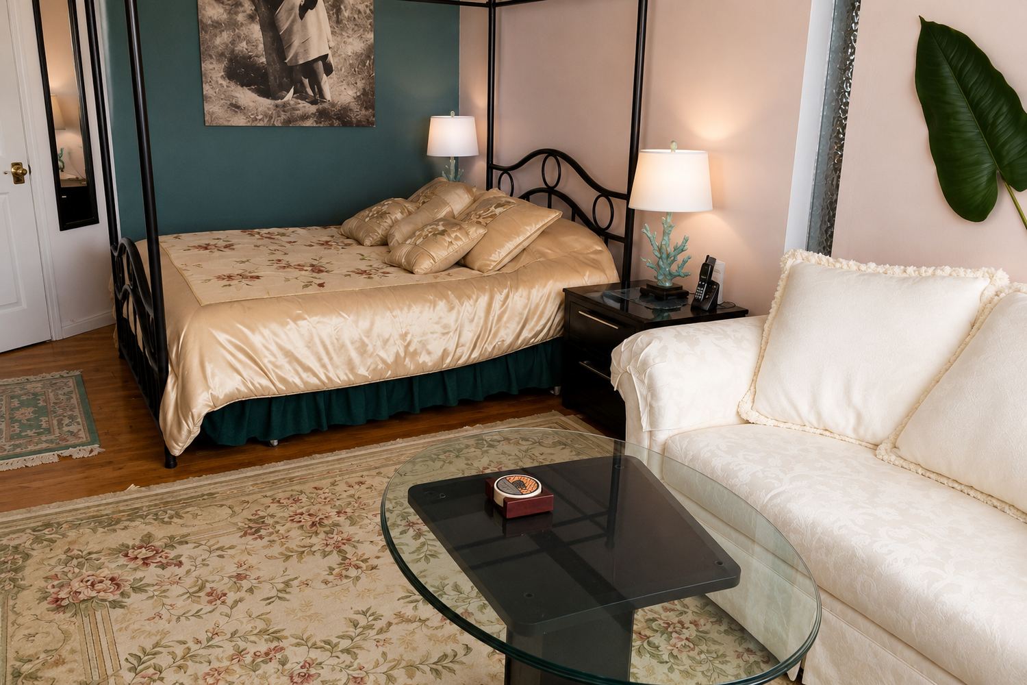 The Den Suite: a queen bed in a black four-poster frame with a gold cover, lamps either side and a cream sofa alongside.