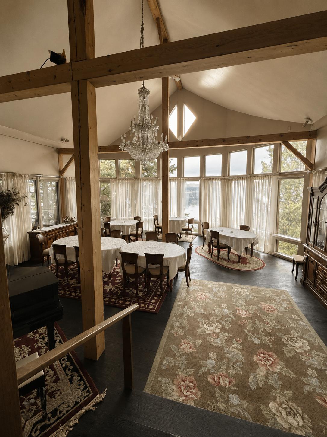 The lakeside dining room, with exposed timber trusses, a crystal chandelier and round tables set under tall windows facing Anahim Lake.